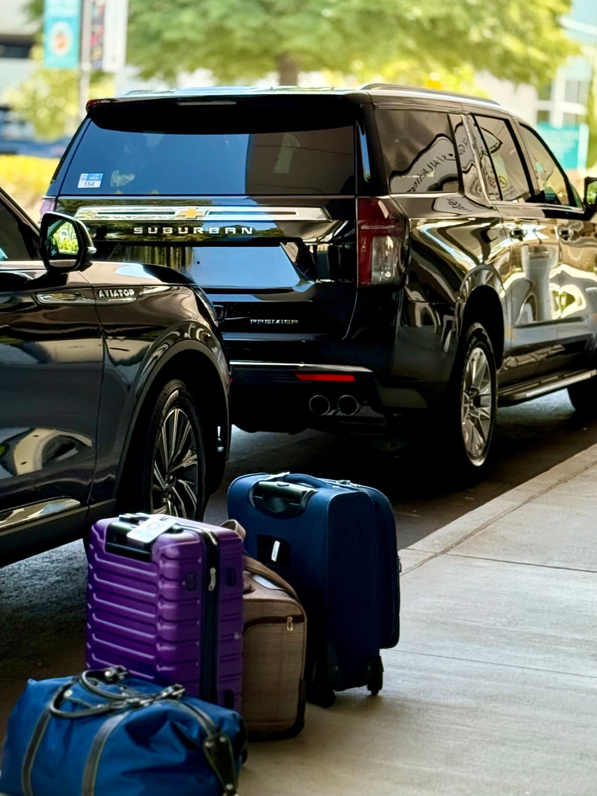 Man in suit, with luggage and bag, looking at phone in hotel lobby; receptionist in background.