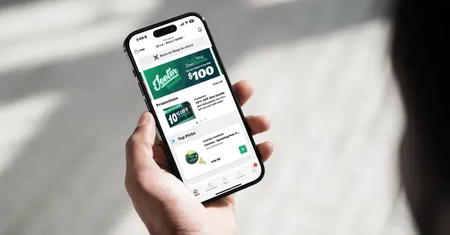 A person holding a smartphone displaying a mobile shopping application with a green and white interface.