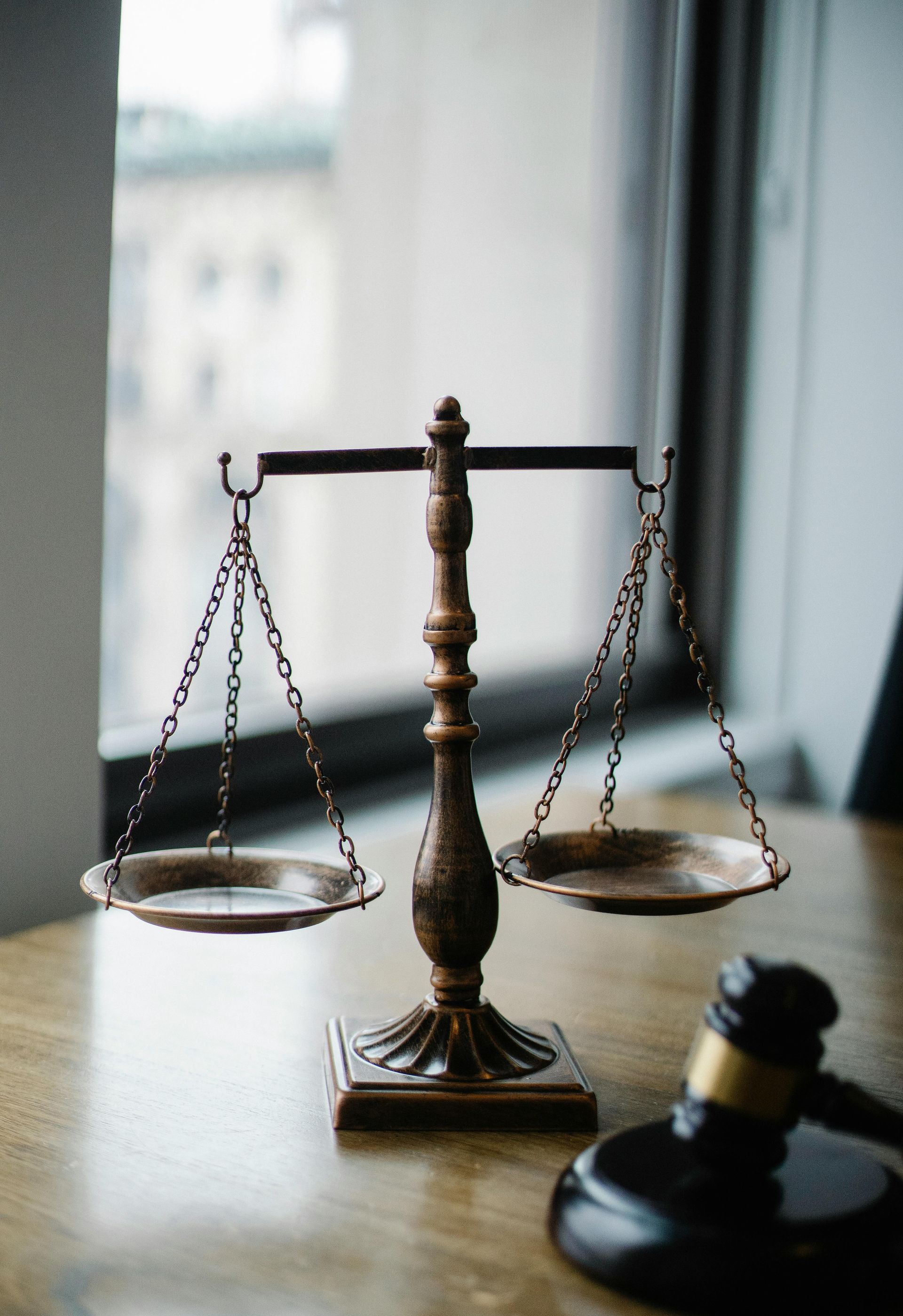Scales of justice and gavel on a wooden table near a window.
