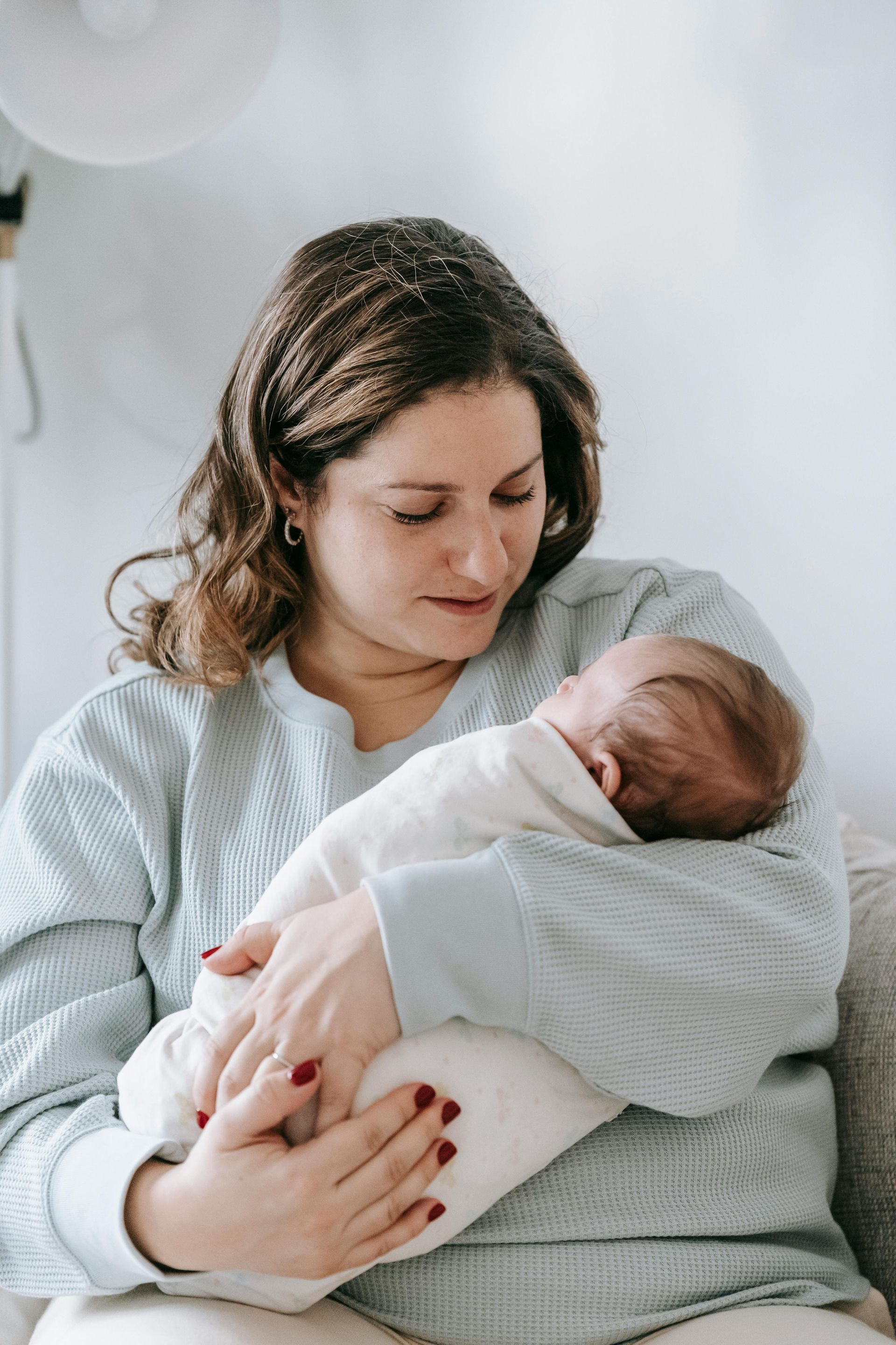 Woman gazing at newborn baby swaddled in white blanket.