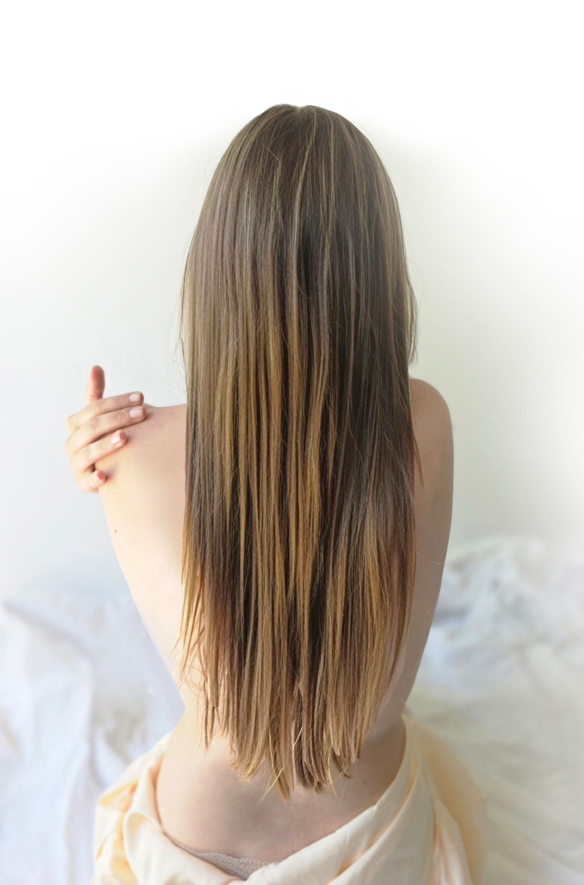 Mujer con cabello largo mojado, de espaldas a la cámara, con los brazos cruzados, envuelta en una sábana.
