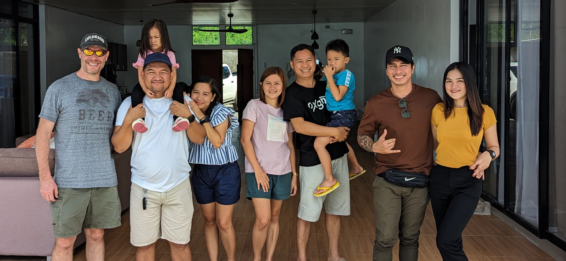 Group of people smiling, posing for photo, inside a home, some are holding children.