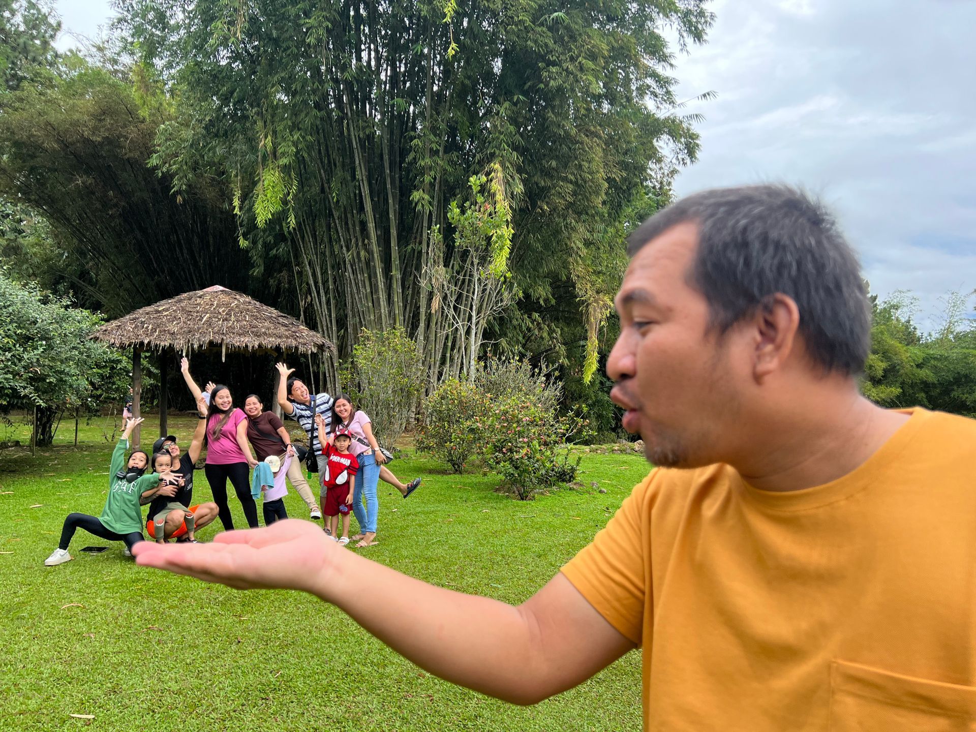 Man with hand out and people in background, outside in a park.