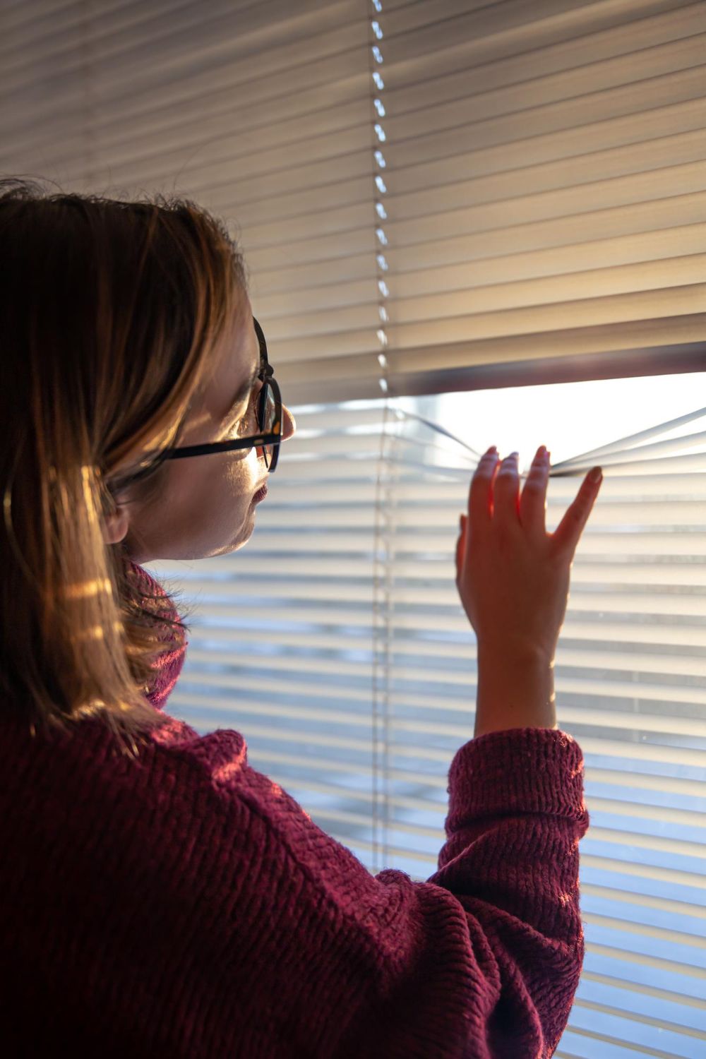 A woman wearing glasses is looking out of a window.