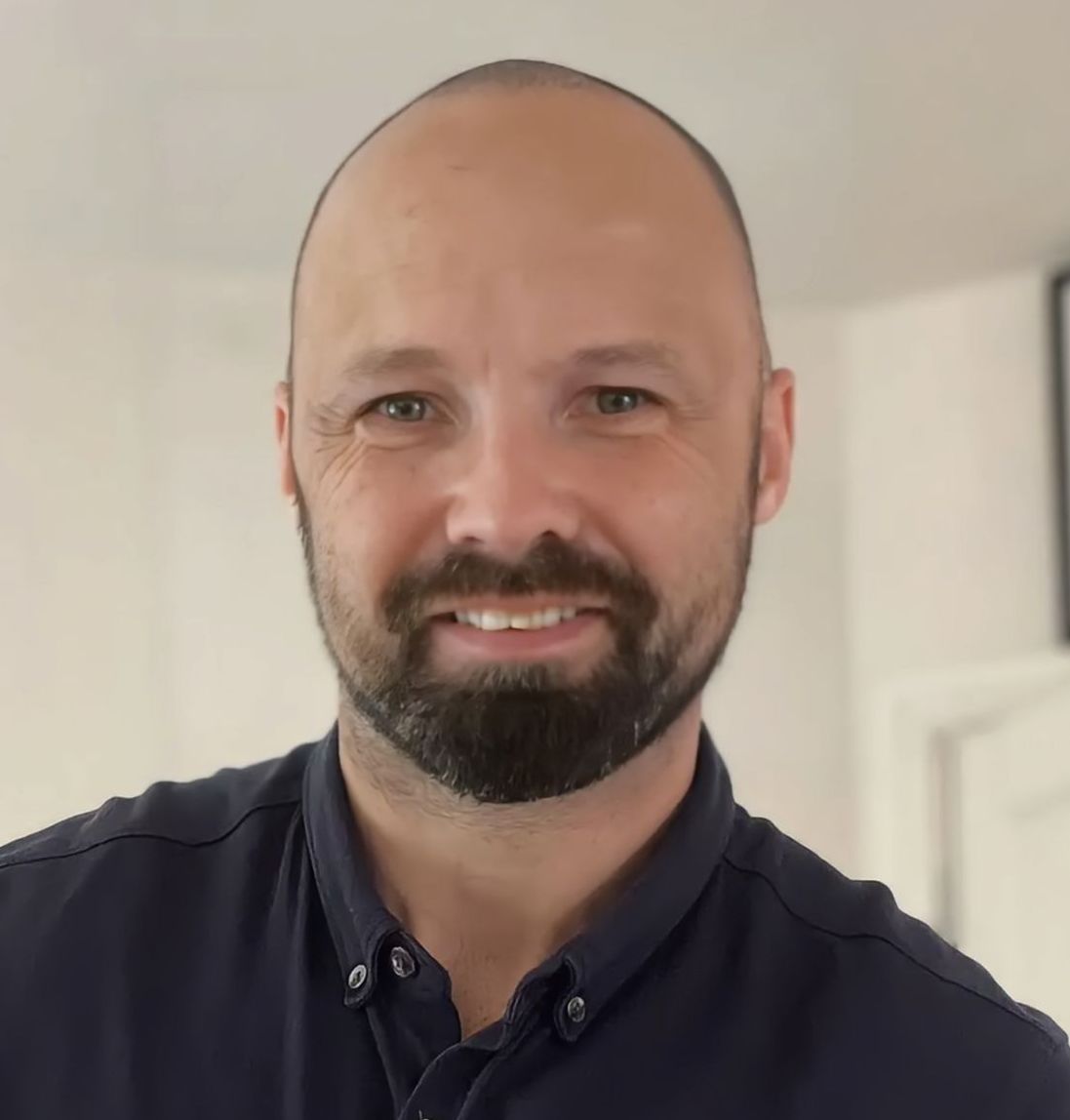 A bald man with a beard is smiling for the camera
