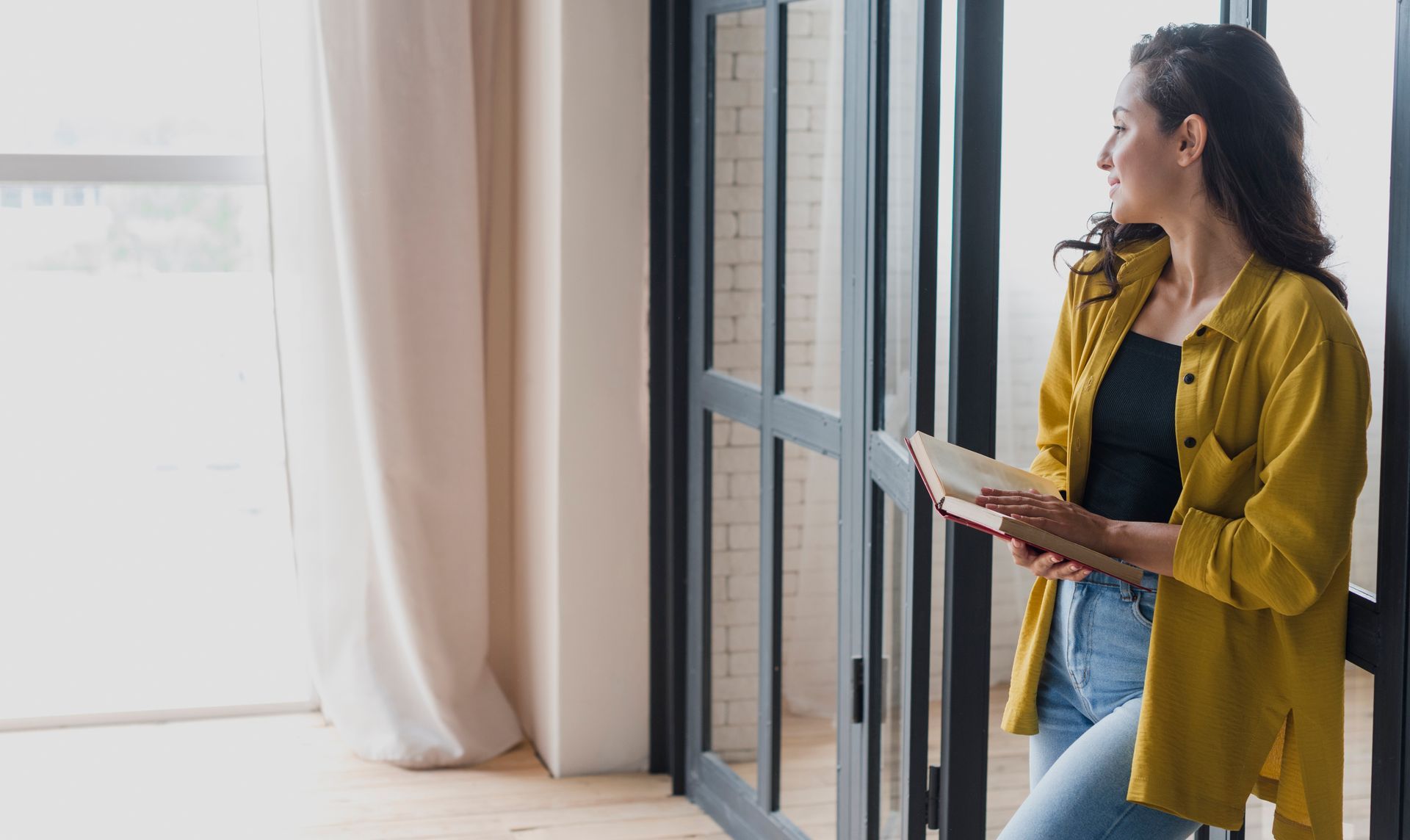 A woman is standing in front of a window holding a book.