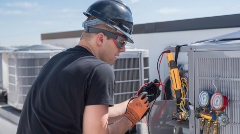 A man wearing a hard hat and safety glasses is working on an air conditioner.