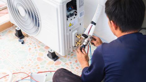 A man is sitting on the floor fixing an air conditioner.