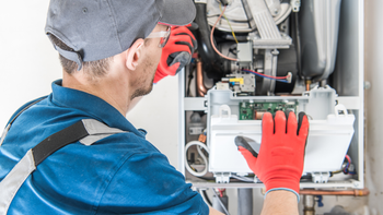 A man wearing red gloves is working on a boiler.