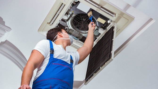 A man wearing a mask is working on an air conditioner.