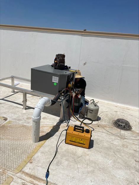 A man is working on an air conditioner on the sidewalk.