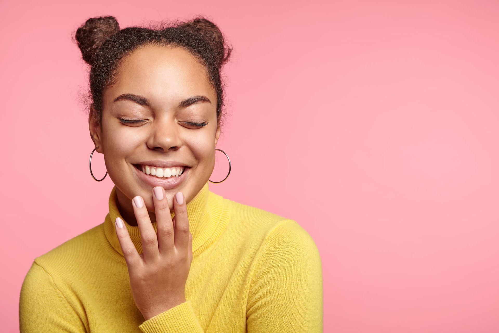 A woman in a yellow sweater is smiling with her eyes closed.