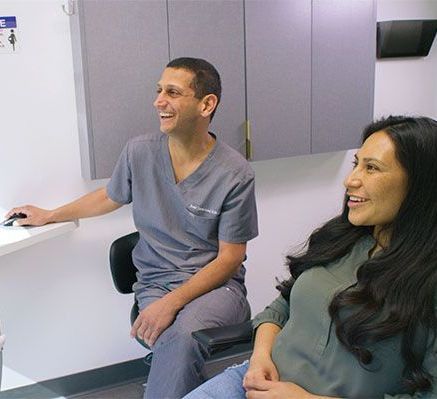 Dr. Jamsheed and a woman are sitting next to each other in a dental office.