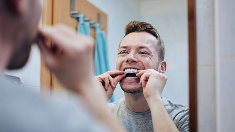 A man is using a whitening tray in front of a mirror.