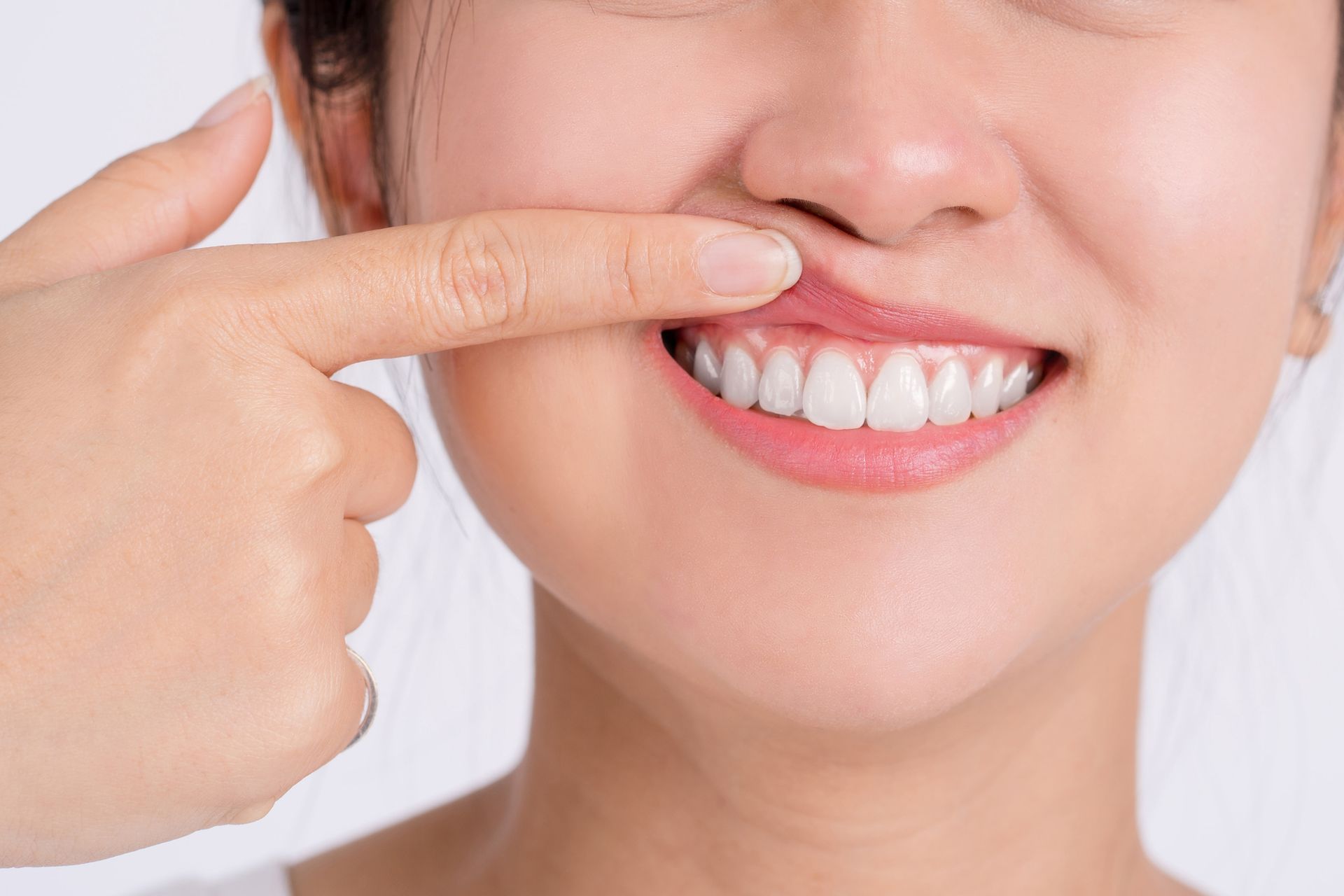 Woman smiling, holding clear aligner in dental office.