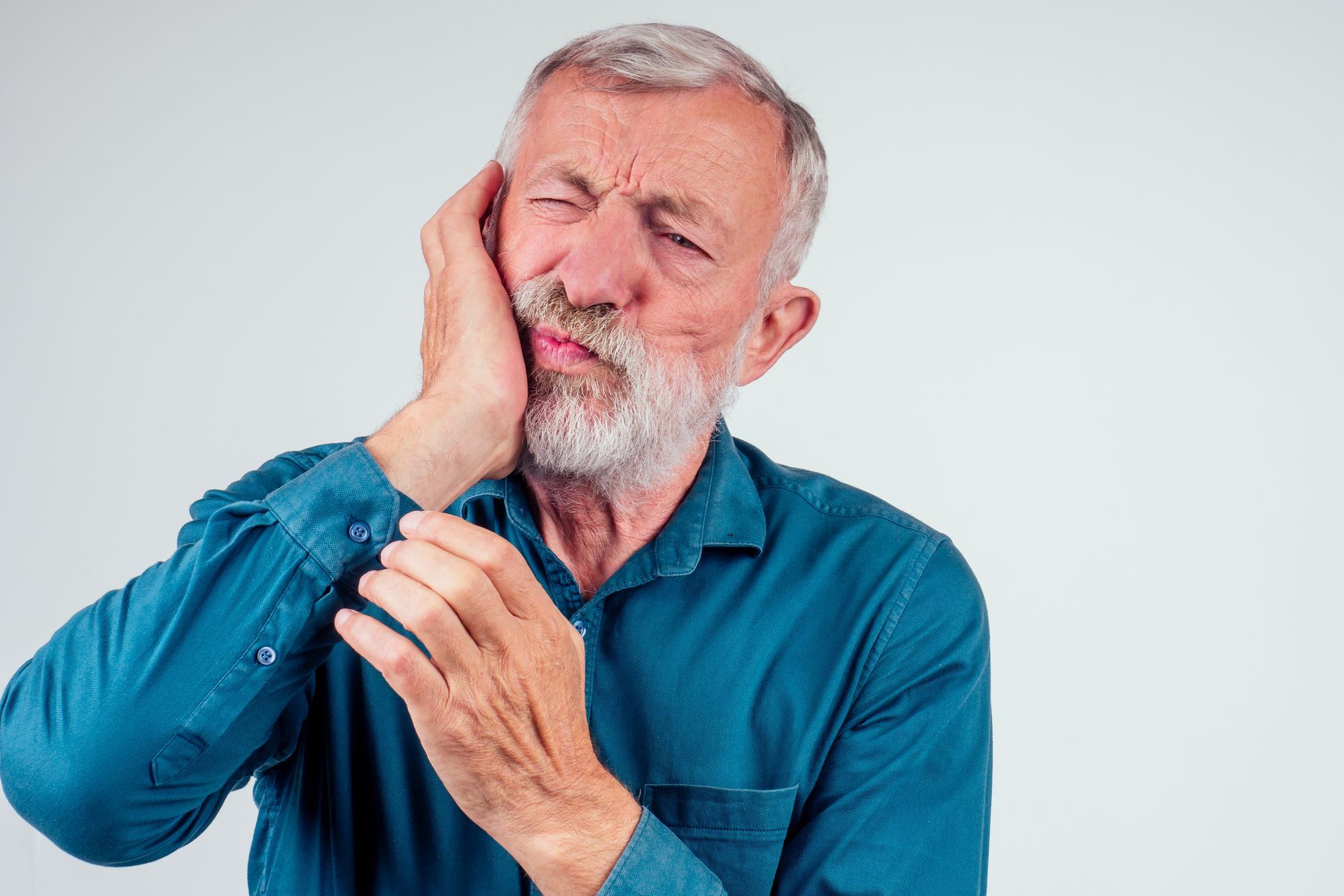 An elderly man with a beard is holding his mouth in pain.