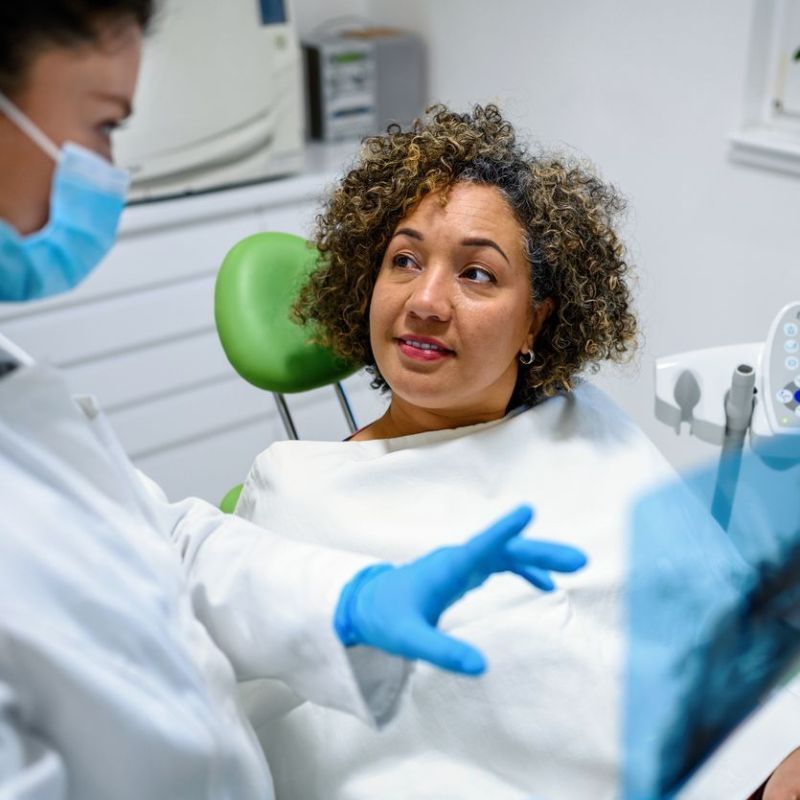 A woman is sitting in a dental chair talking to a dentist.