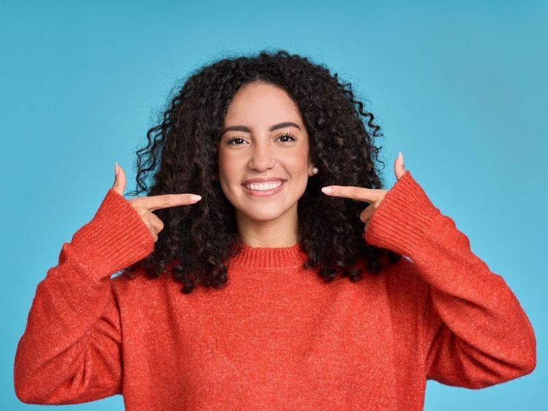 A woman in a red sweater is pointing at her teeth.