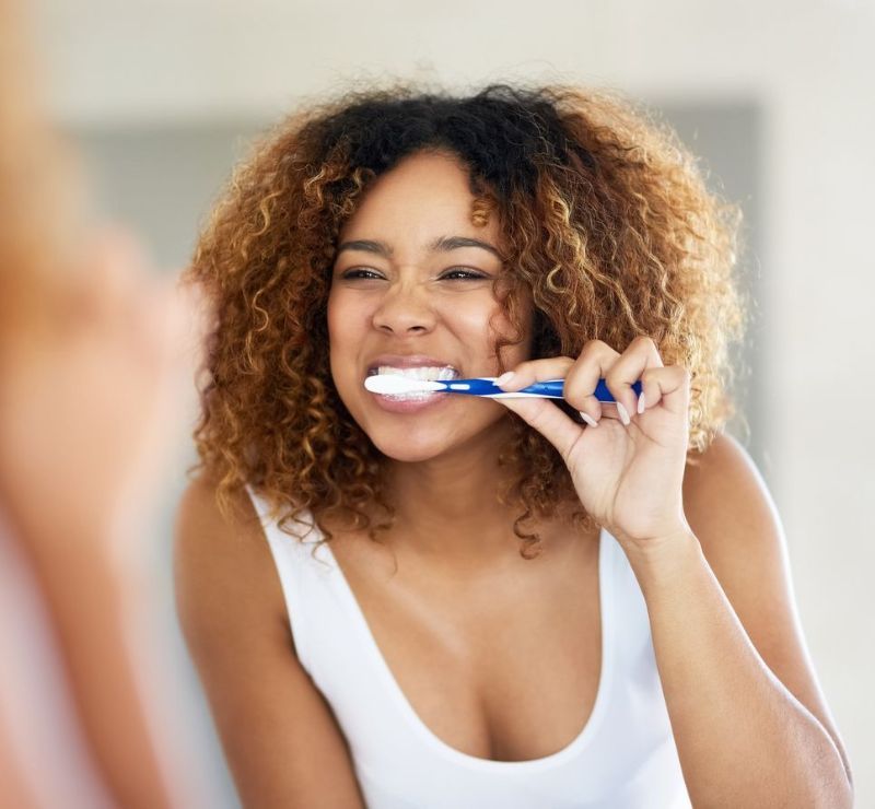 A woman is brushing her teeth in front of a mirror.