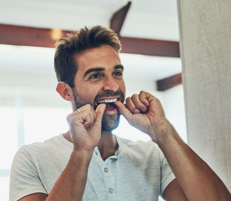 A man is flossing his teeth in front of a mirror.