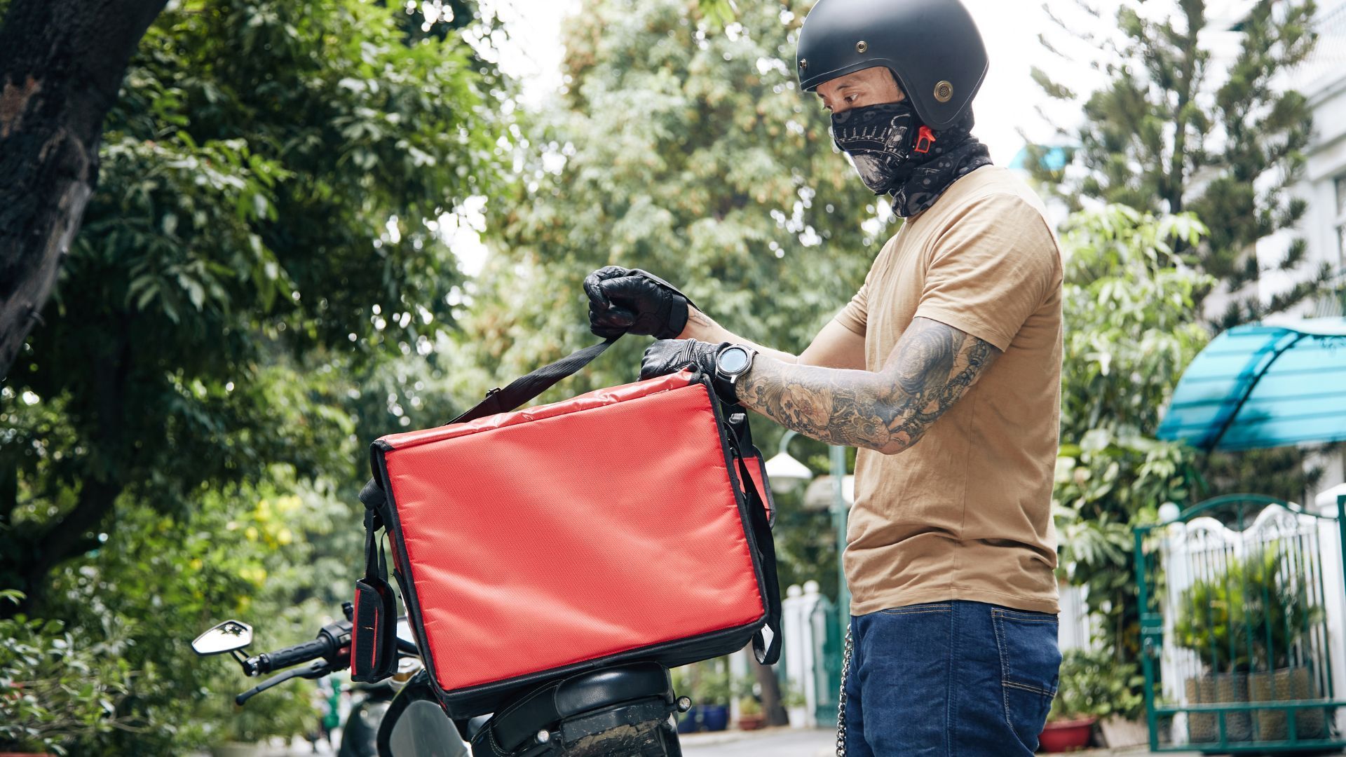 Person in a helmet loads a red delivery box onto a bicycle outdoors.