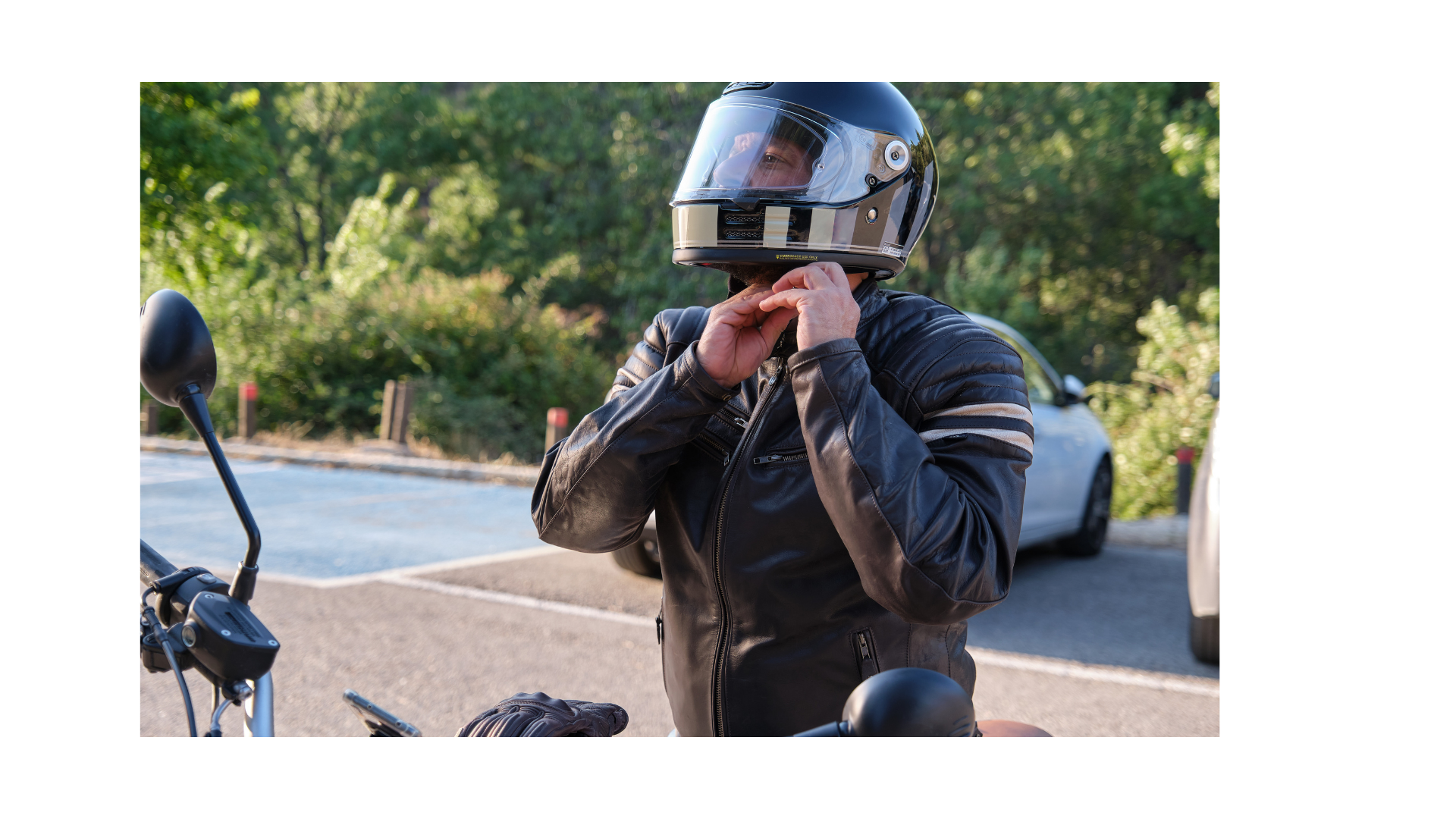 Motorcyclist in black gear adjusting helmet on a roadside with trees in the background