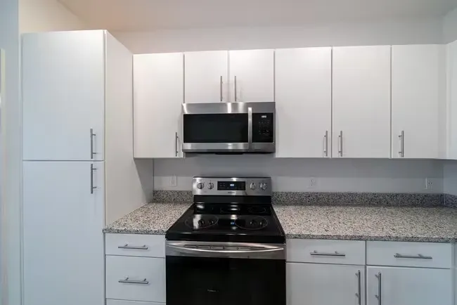 White kitchen with a microwave, stove, cabinets, and granite countertop.
