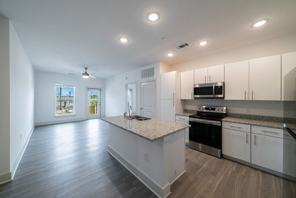 Modern kitchen and living area with island, white cabinets, stainless steel appliances, and gray floors.