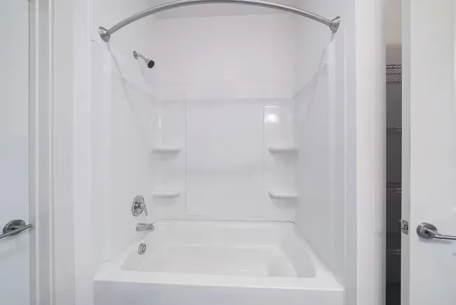 White bathroom with a tub, shower head, and shelving.