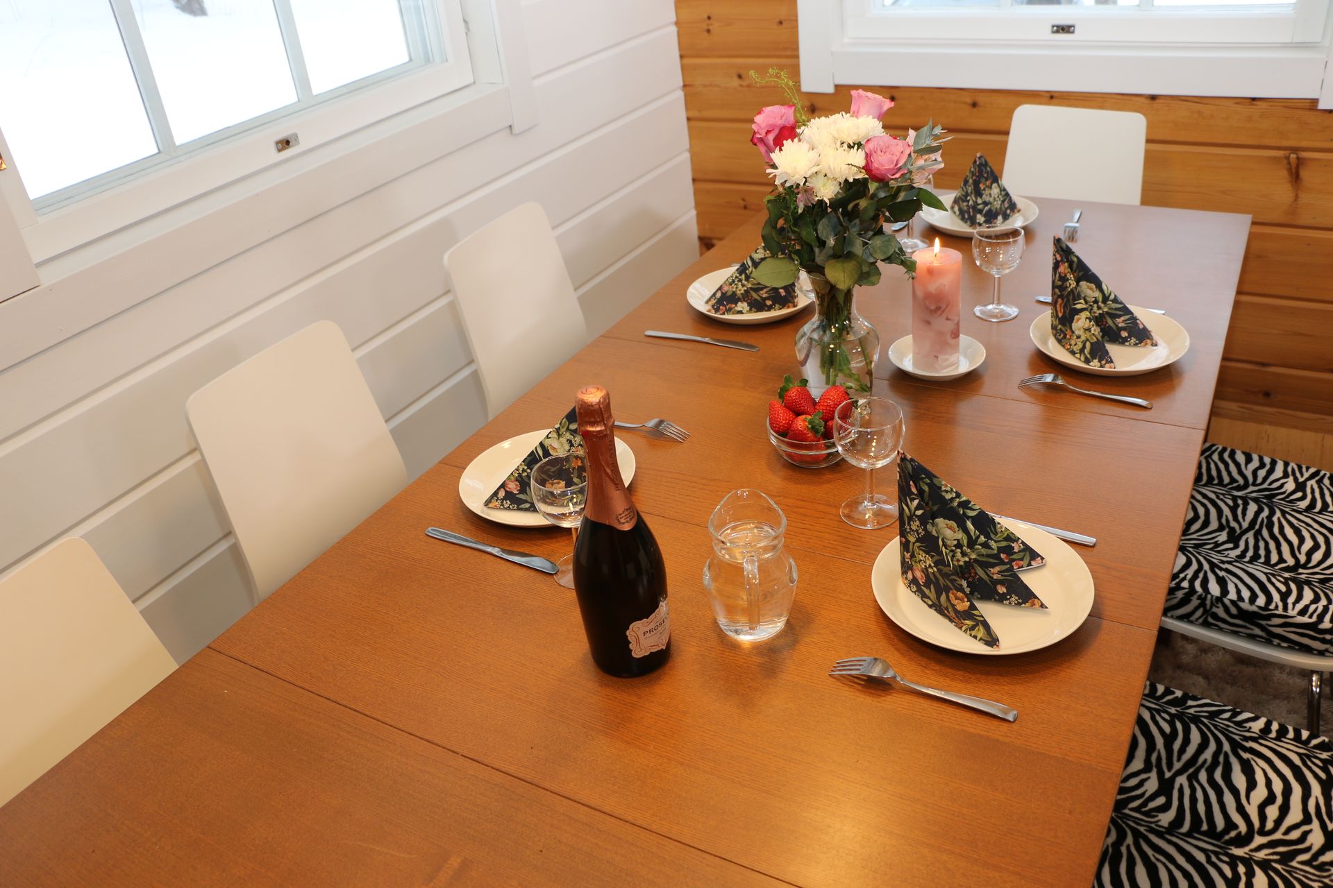 A bottle of champagne sits on a table with plates and utensils.