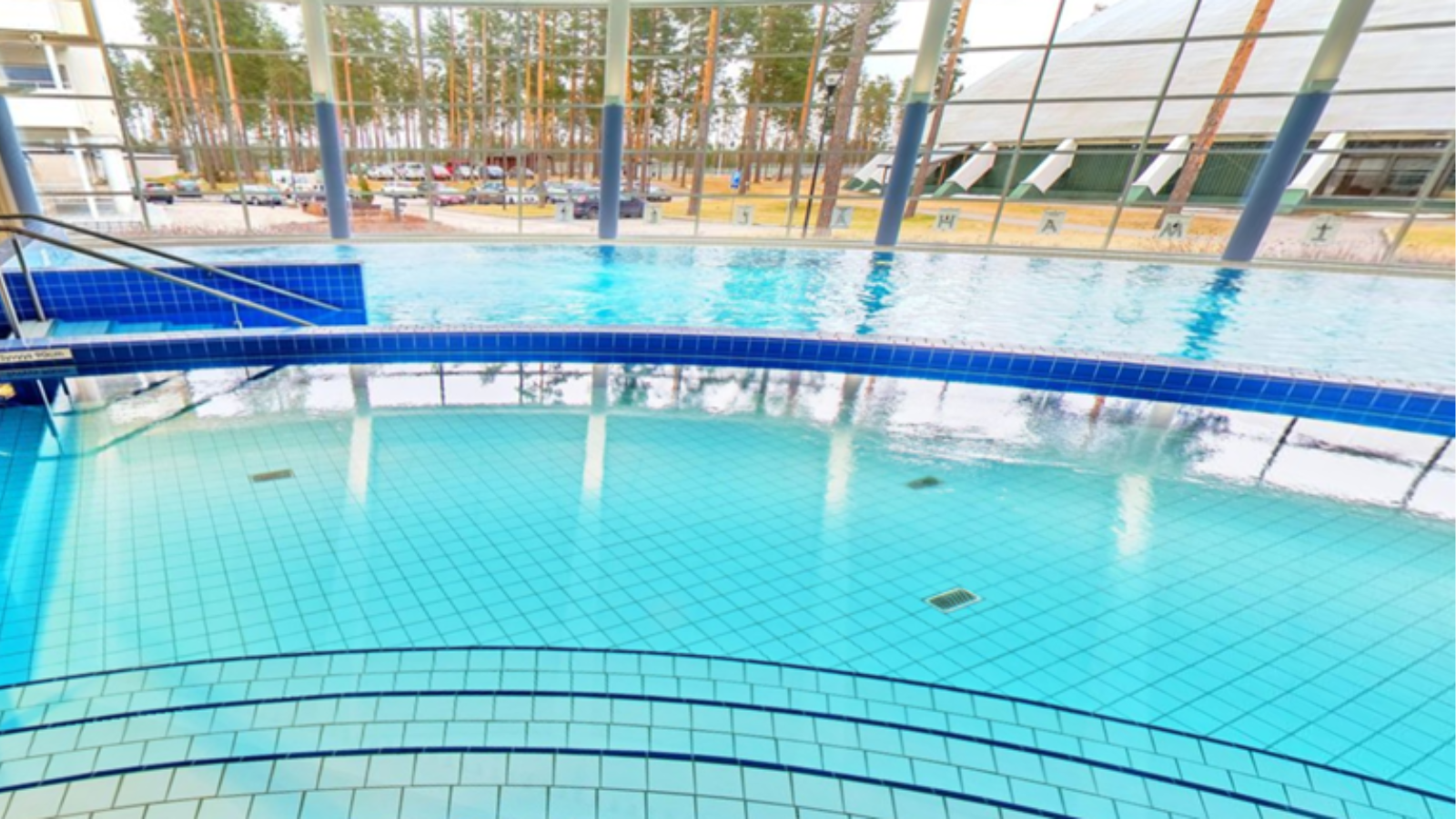 A large indoor swimming pool with blue tiles and stairs leading to it.