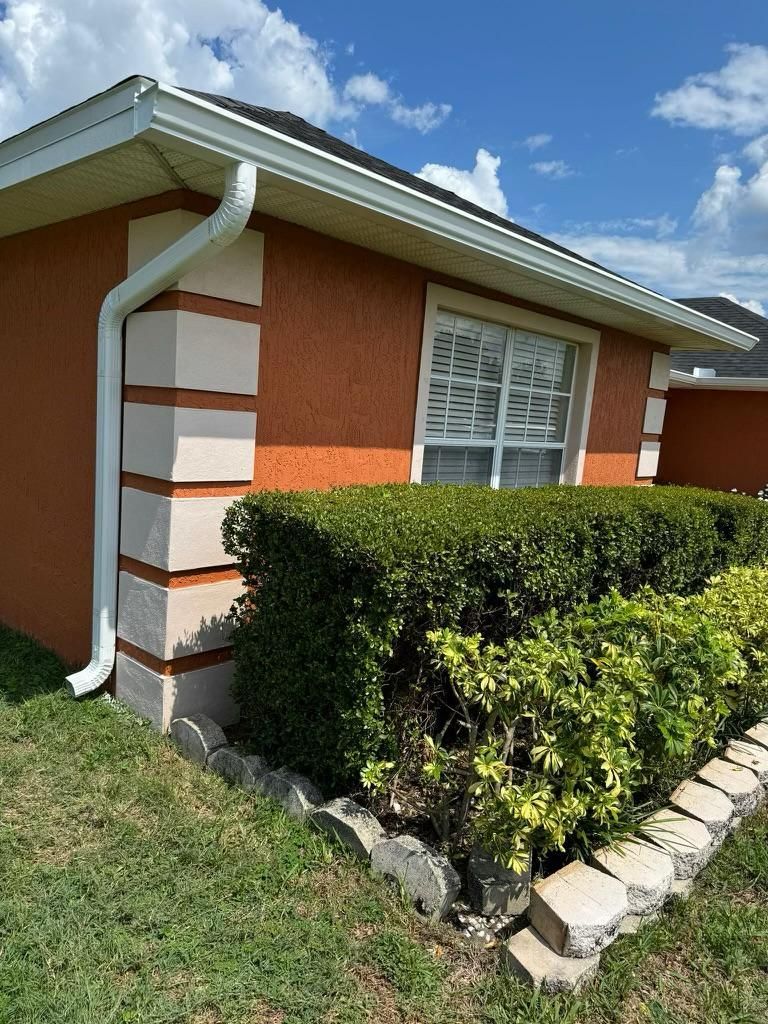 A house with a gutter on the side of it and a hedge in front of it.