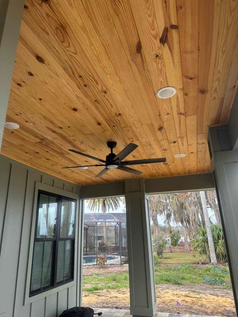 A porch with a wooden ceiling and a ceiling fan.