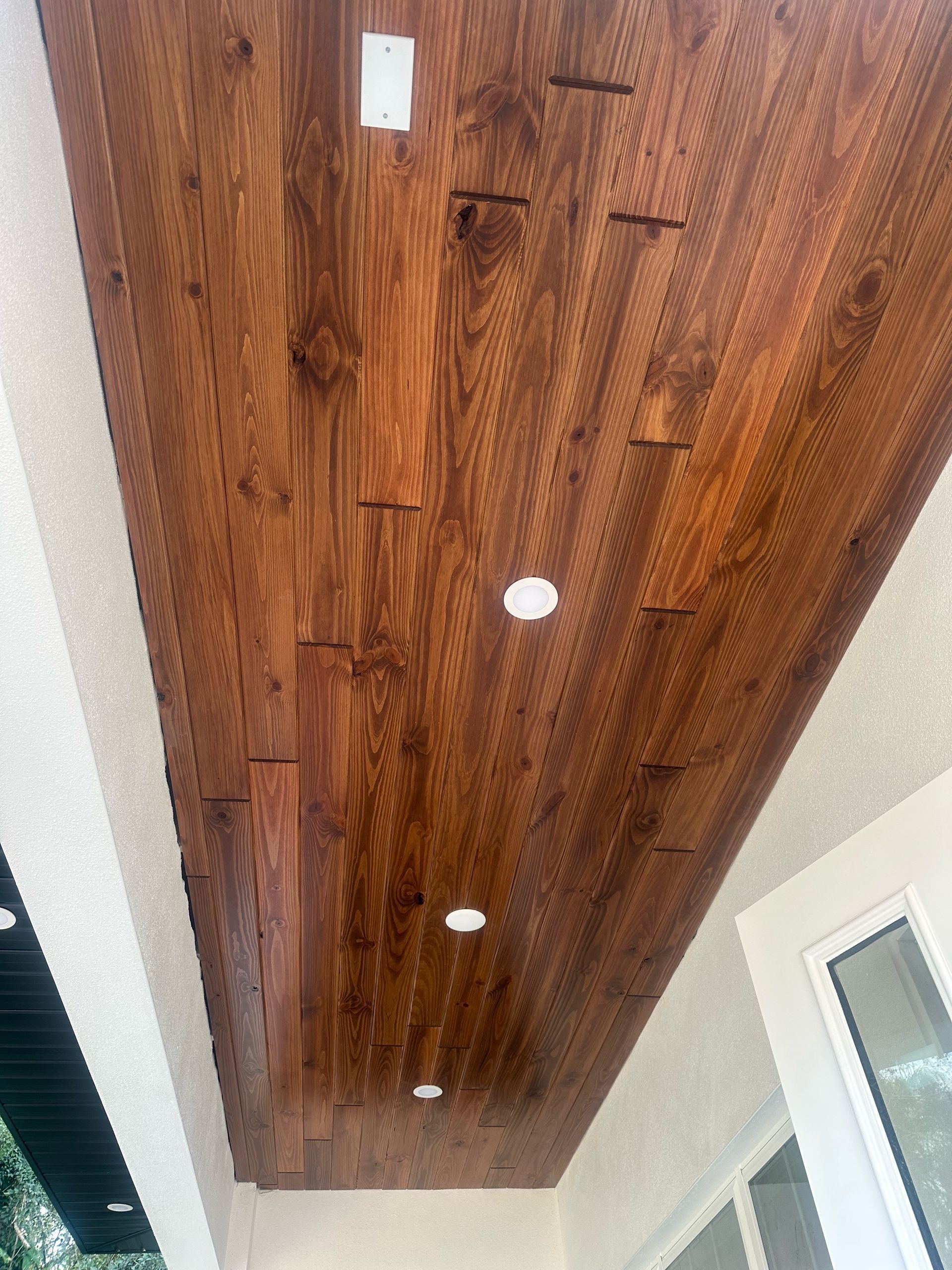 A wooden ceiling with lights on it is on a porch.
