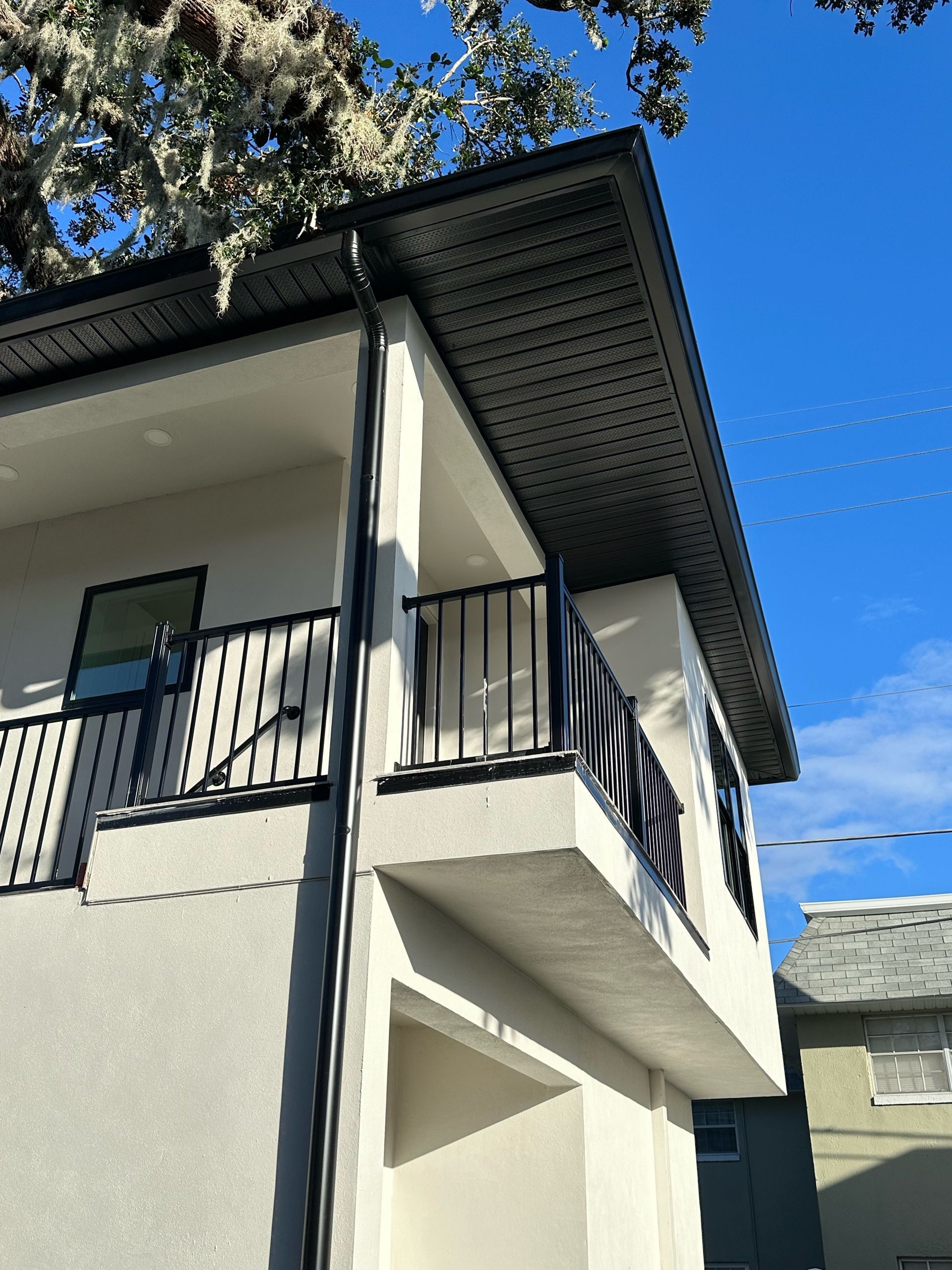 A white house with a balcony and a tree in the background