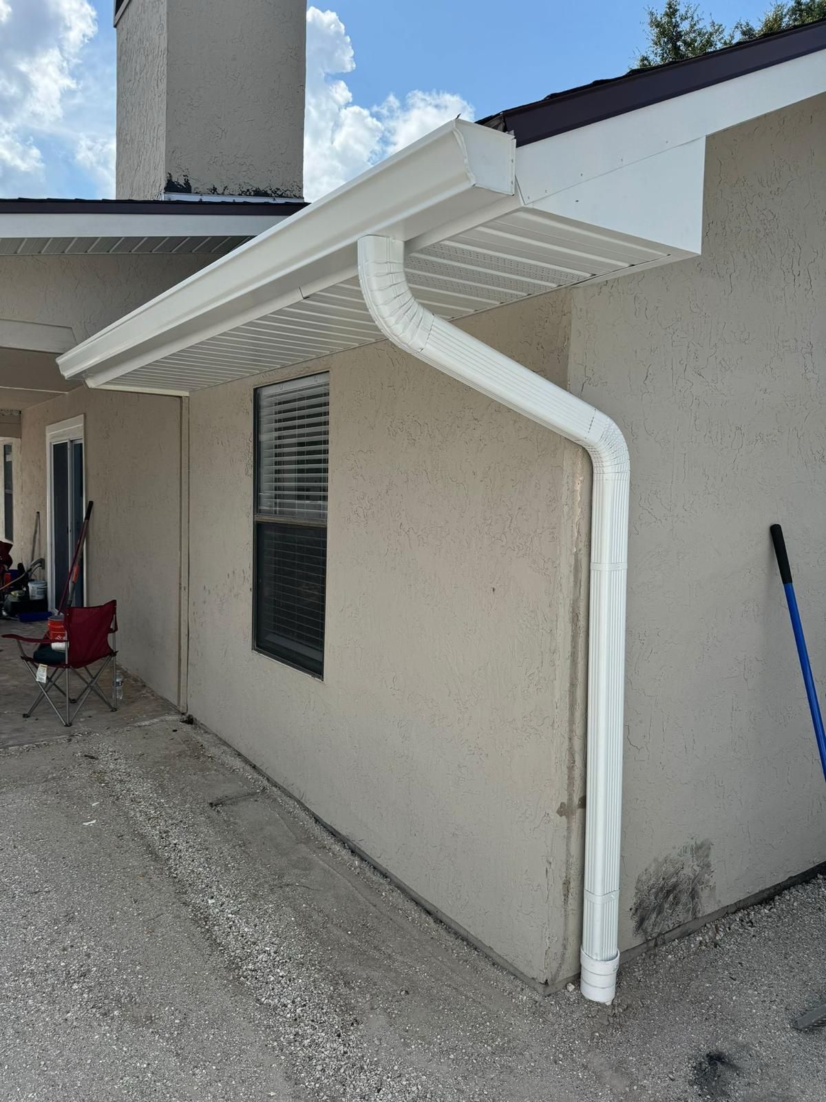 A white gutter on the side of a house next to a window.