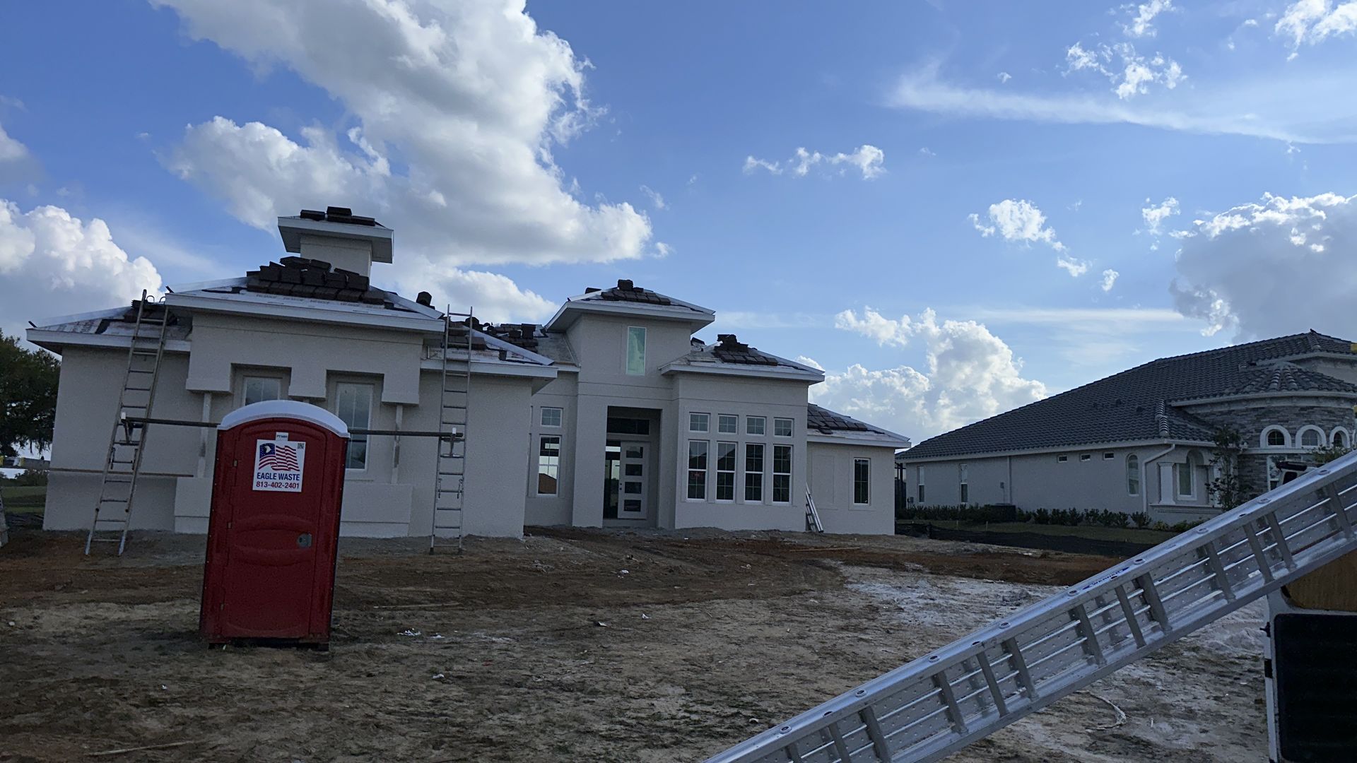 A large white house under construction with a red portable toilet in front of it.