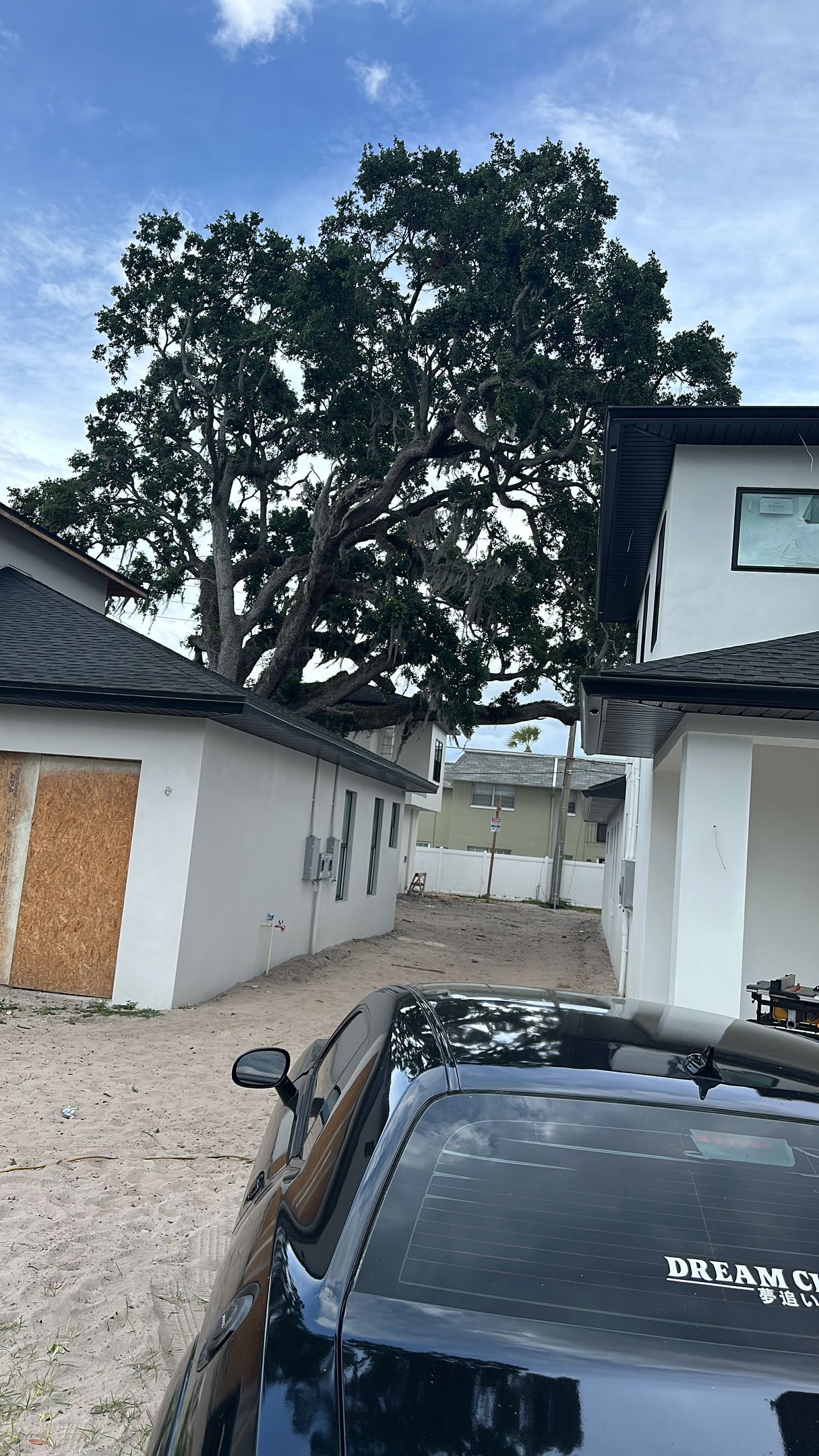 A black car is parked in front of a house with a tree in the background.
