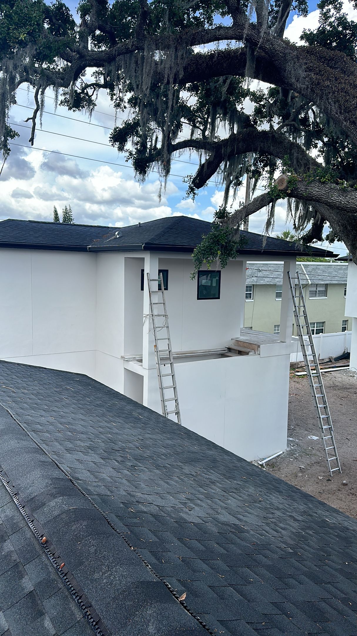 A white house with a black roof and a ladder on the roof.