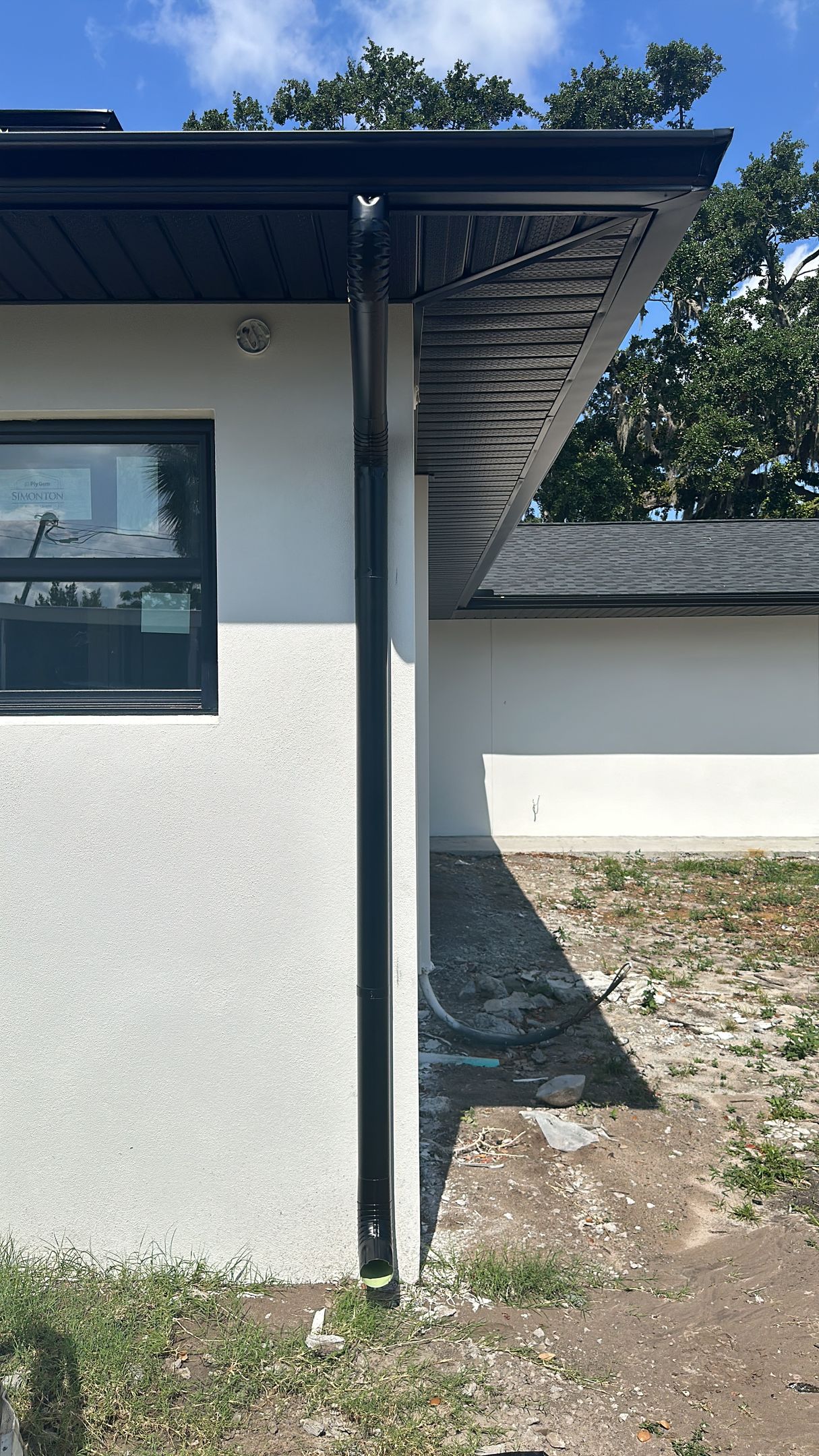 A white house with a black gutter on the side of it.