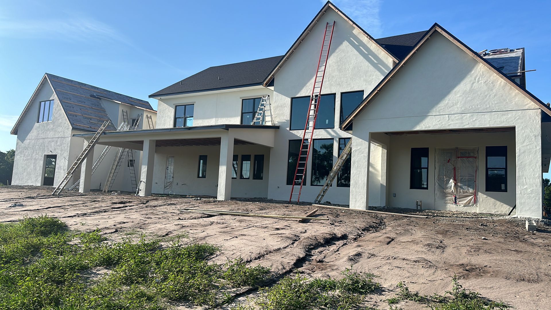 A large white house is being built in a dirt field.