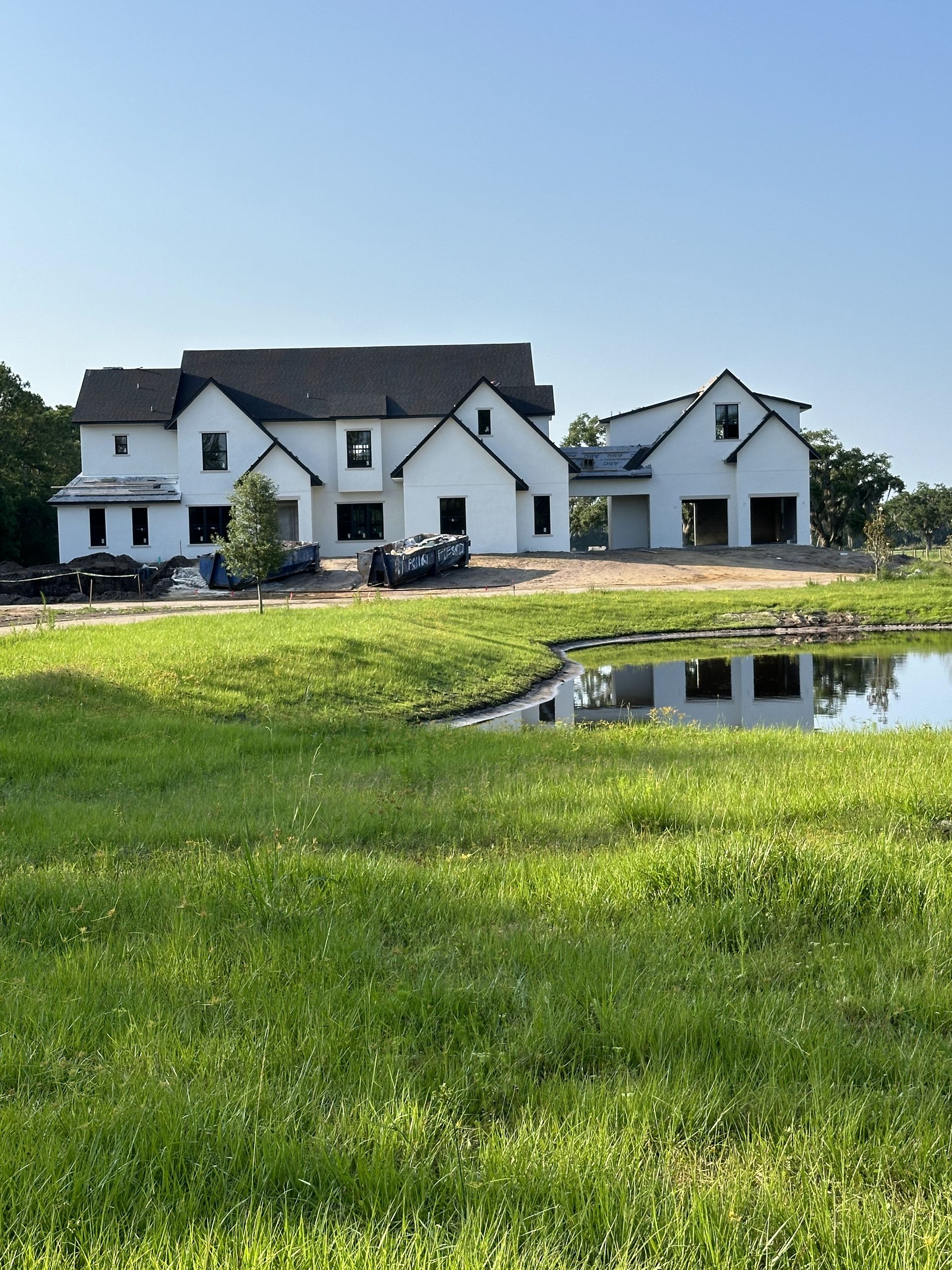 A large white house is sitting in the middle of a lush green field.