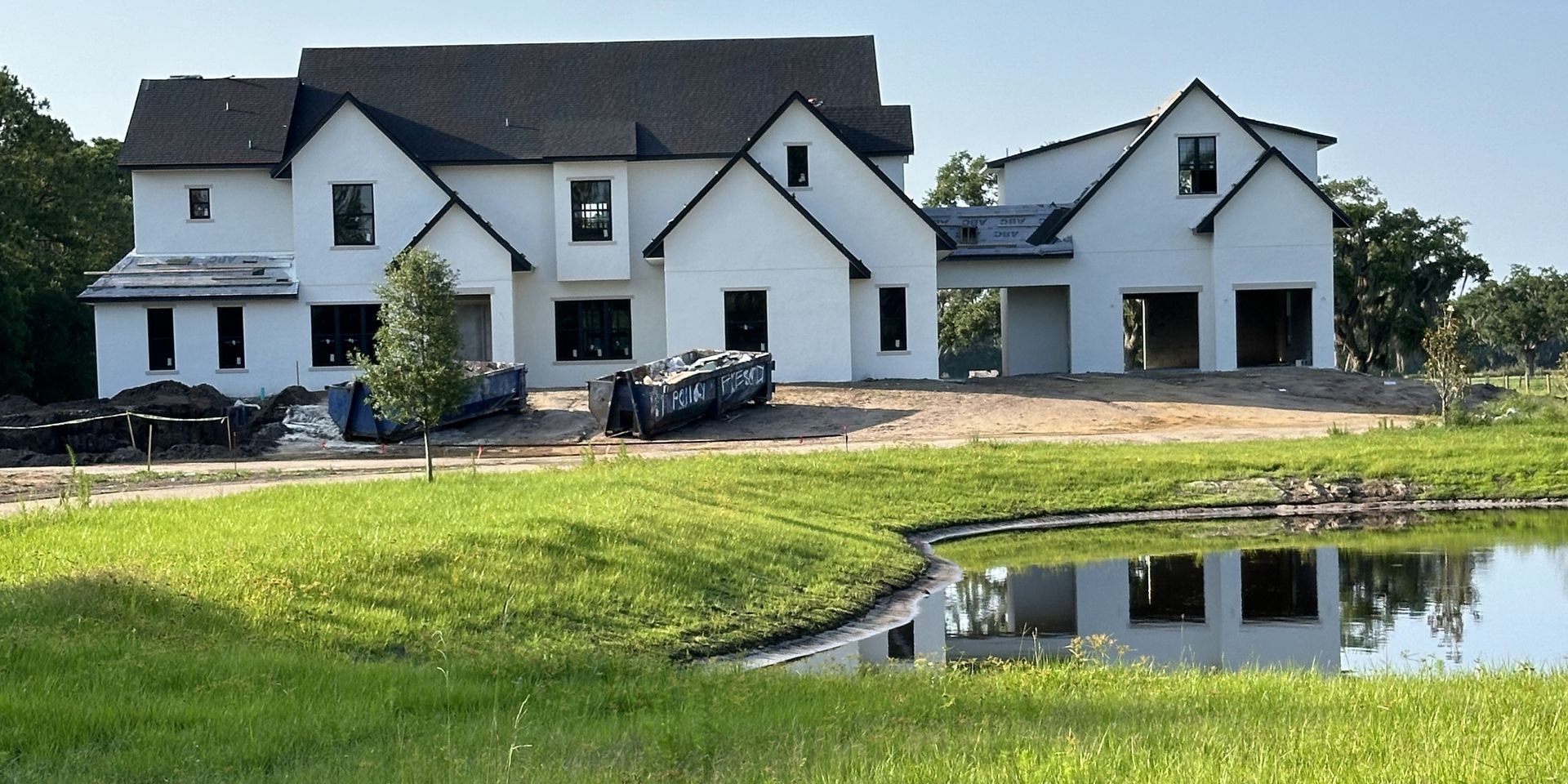A large white house is being built next to a pond