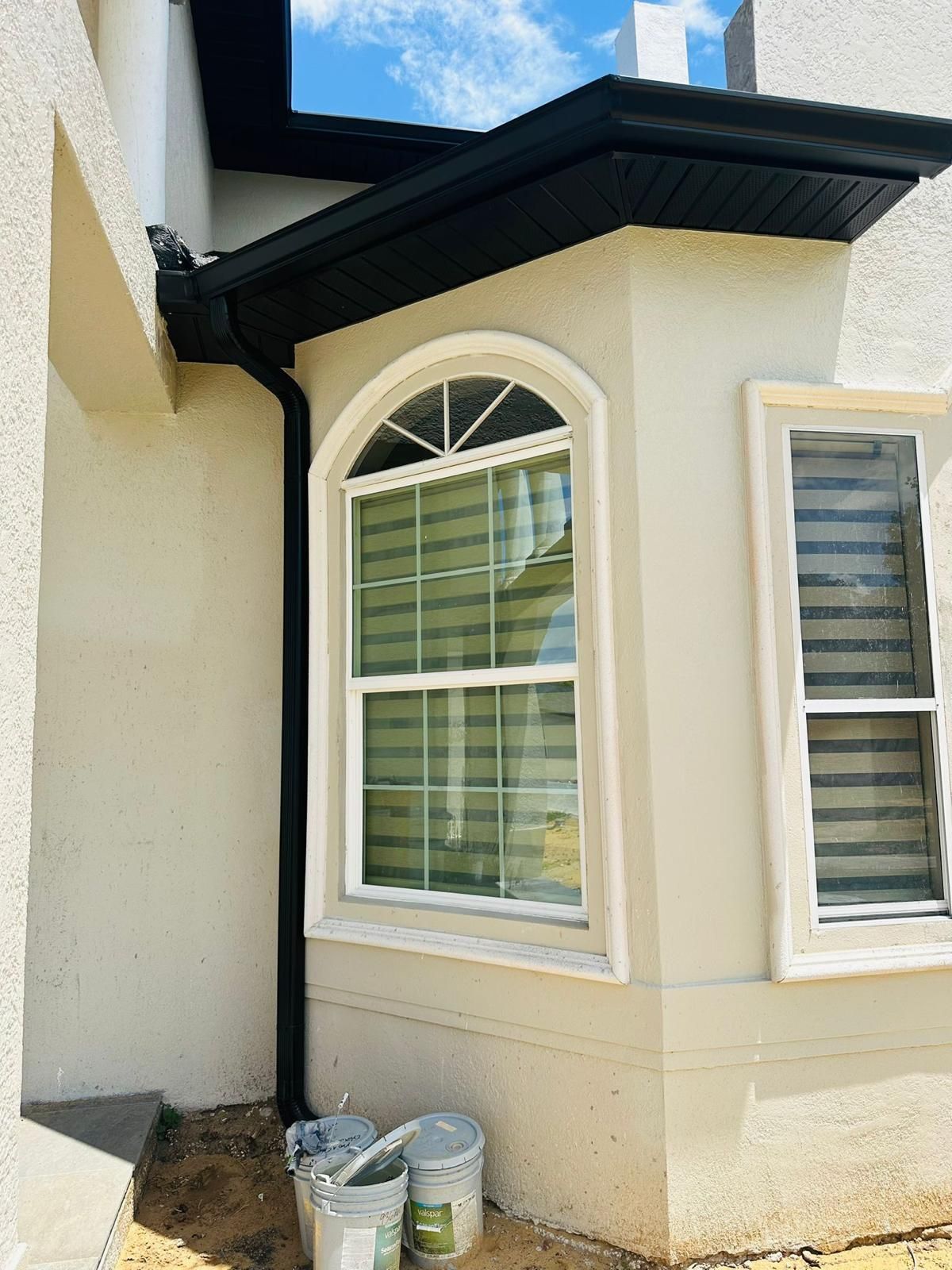 A white house with a large window and a black gutter.