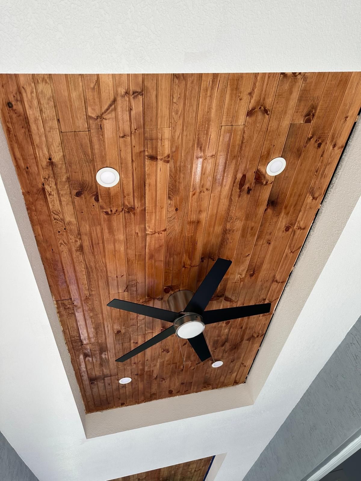 A ceiling fan is hanging from the ceiling of a room with wood paneling.