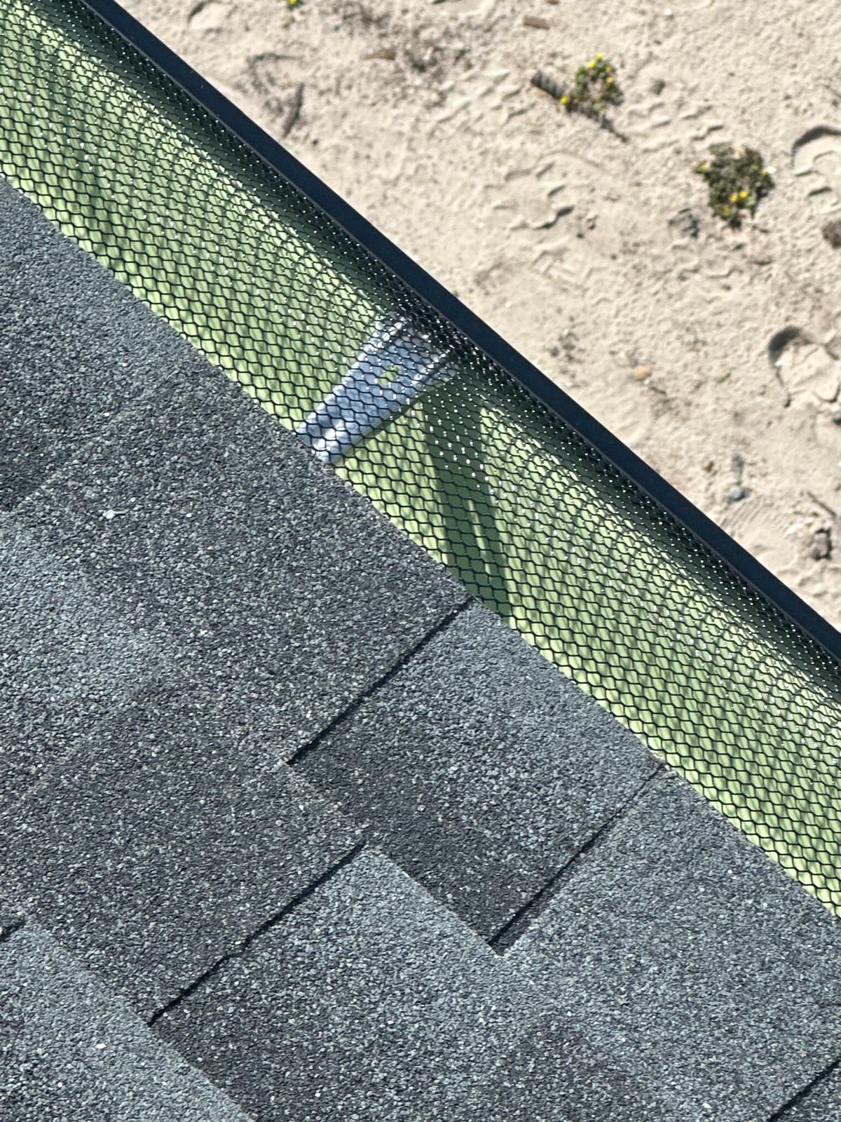 A close up of a roof with shingles and a green gutter.