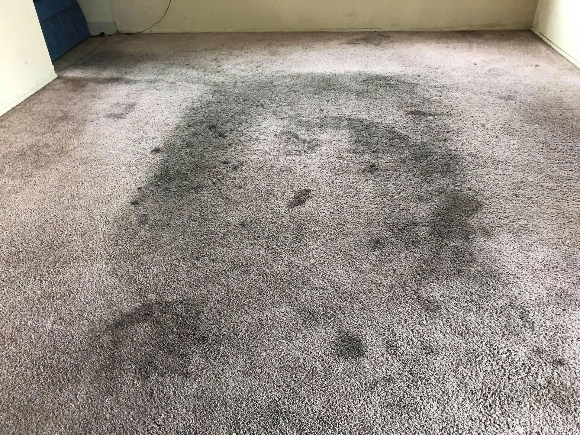 A dirty carpet in a living room with a stain on it.