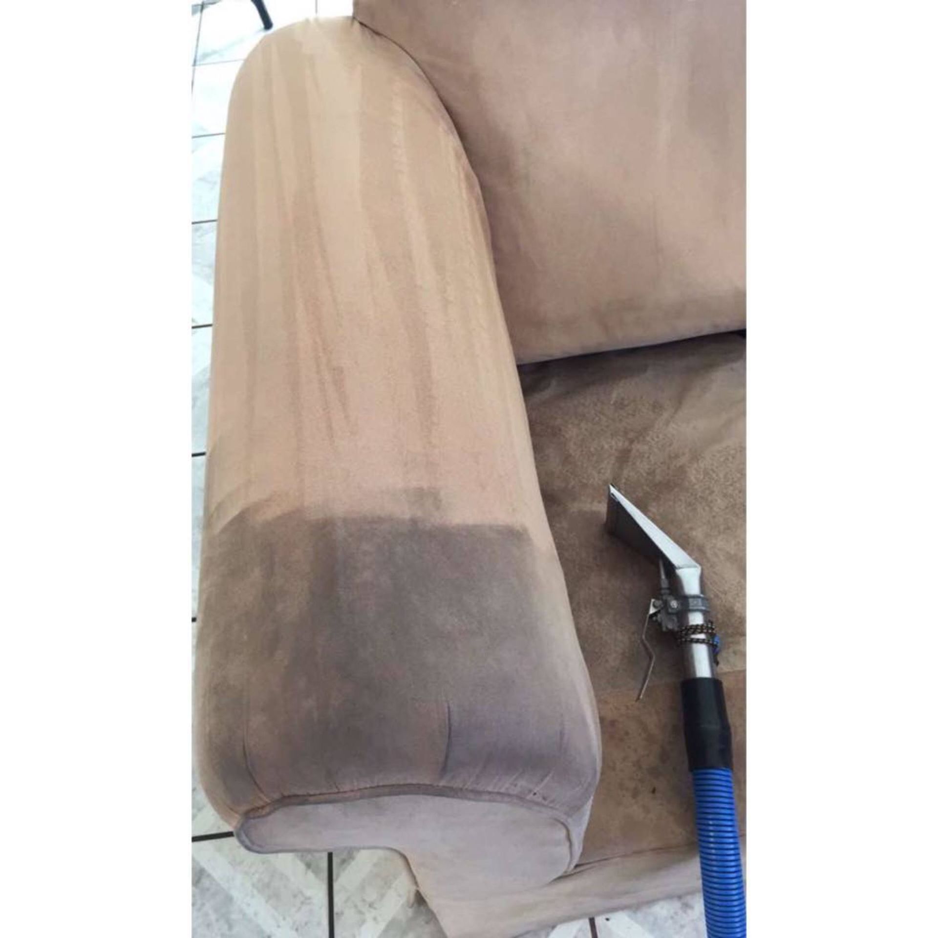 The arm of a couch is being cleaned with a vacuum cleaner.
