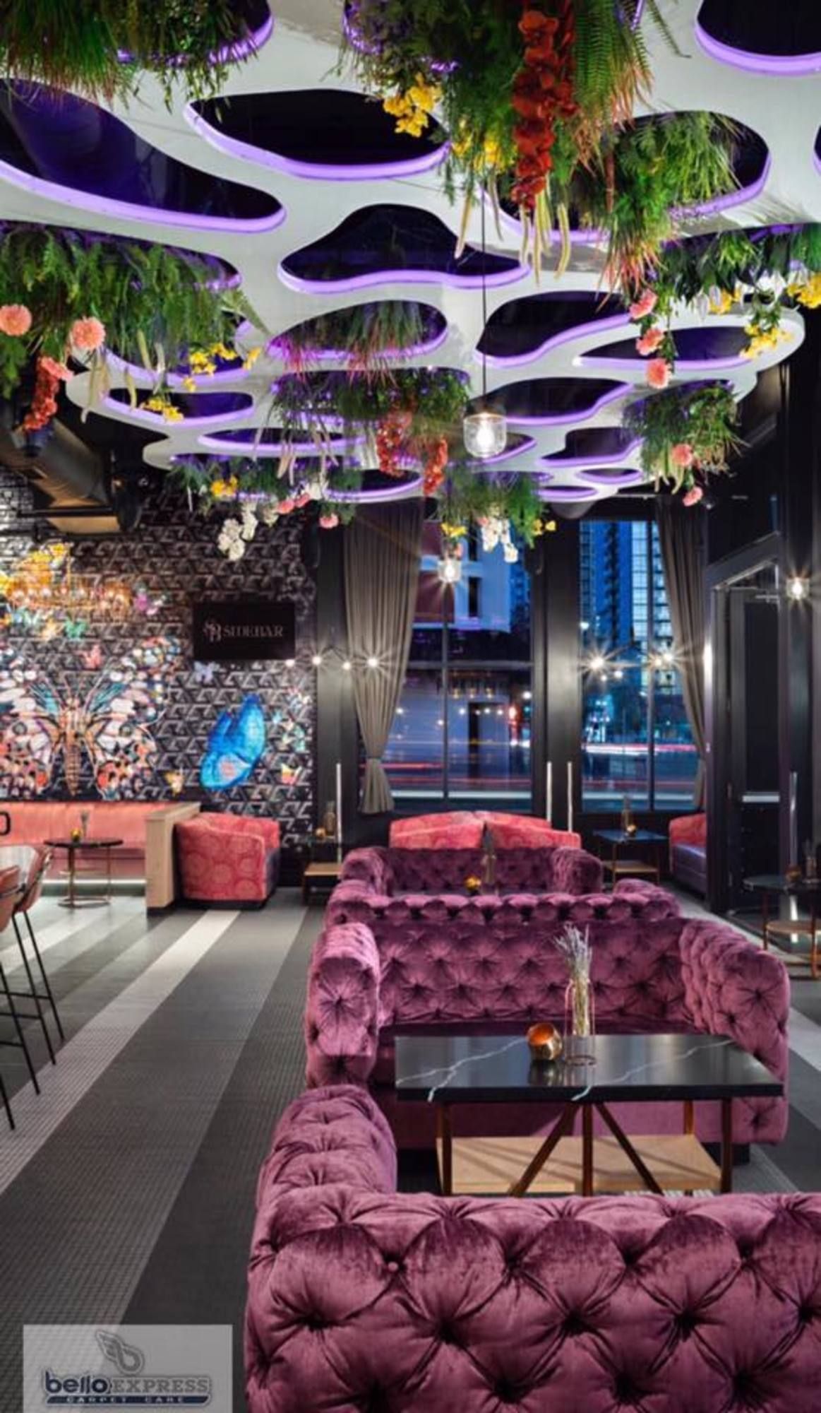 A restaurant with purple furniture and flowers hanging from the ceiling.