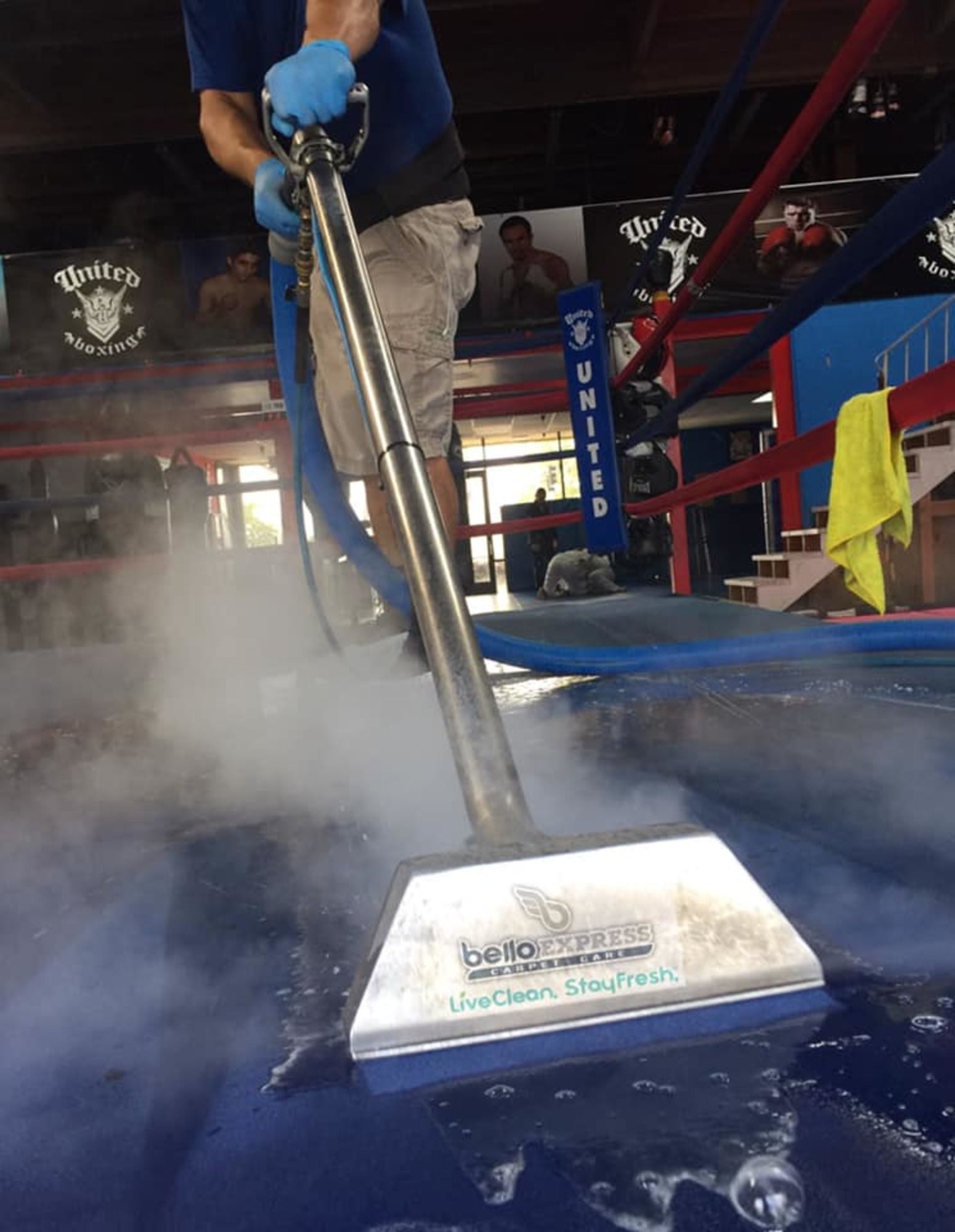 A man is cleaning a blue carpet with a vacuum cleaner.